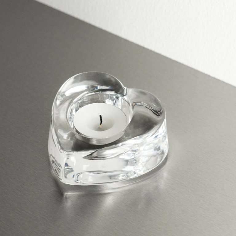 Heart-shaped crystal candle holder with a candle on a reflective surface